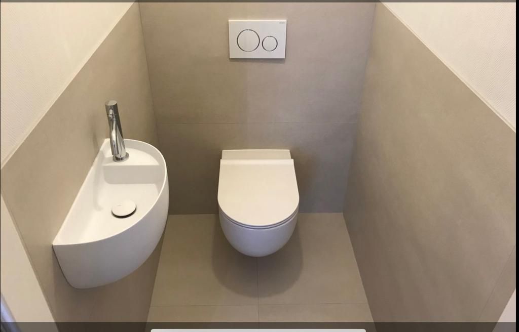 Petite salle de bain moderne avec toilettes suspendues et lavabo. Murs beiges et carrelage au sol.