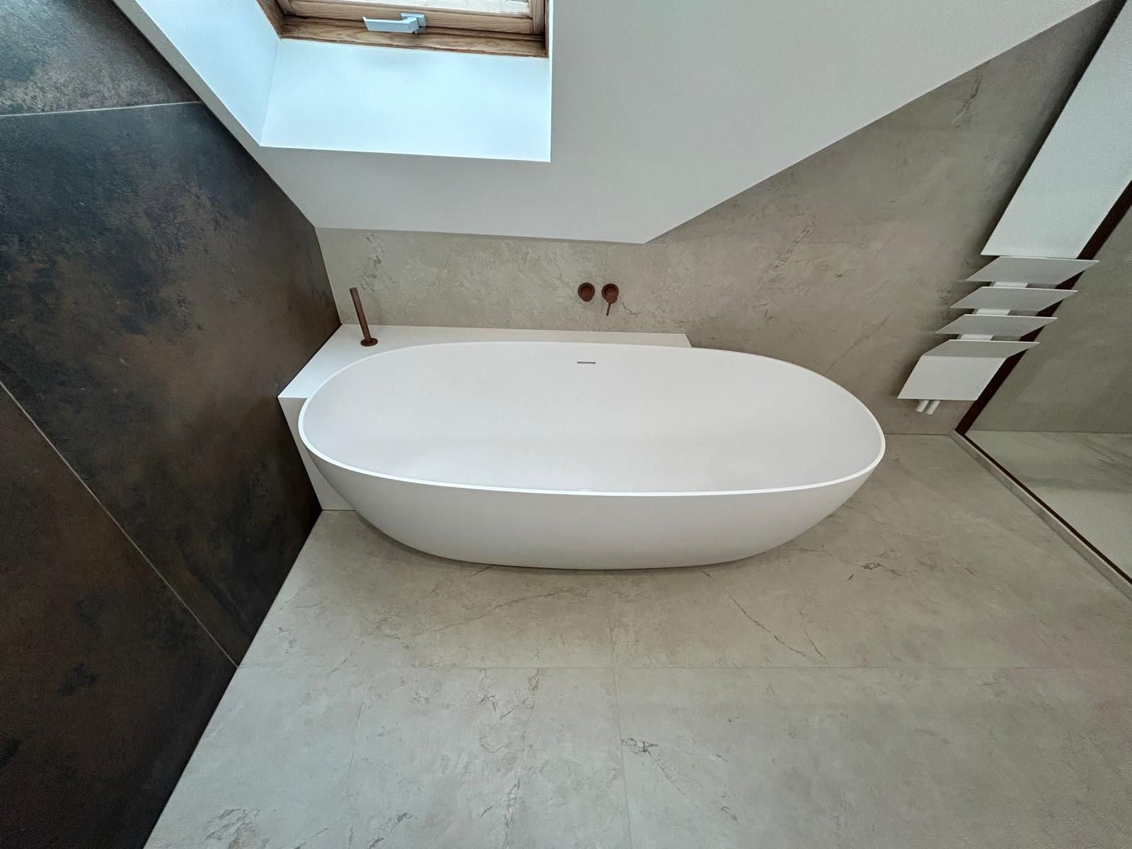 Une baignoire ovale blanche dans une salle de bain moderne avec des murs gris clair et un plafond incliné.