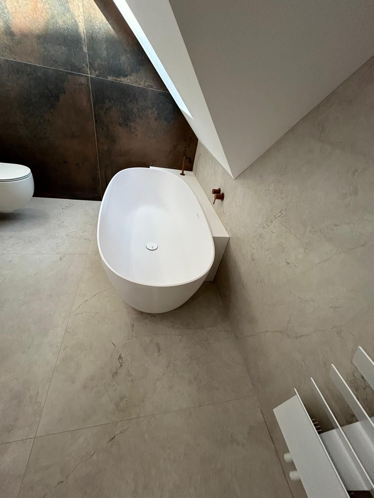 Baignoire blanche autoportante dans une salle de bain avec carrelage neutre et plafond incliné.