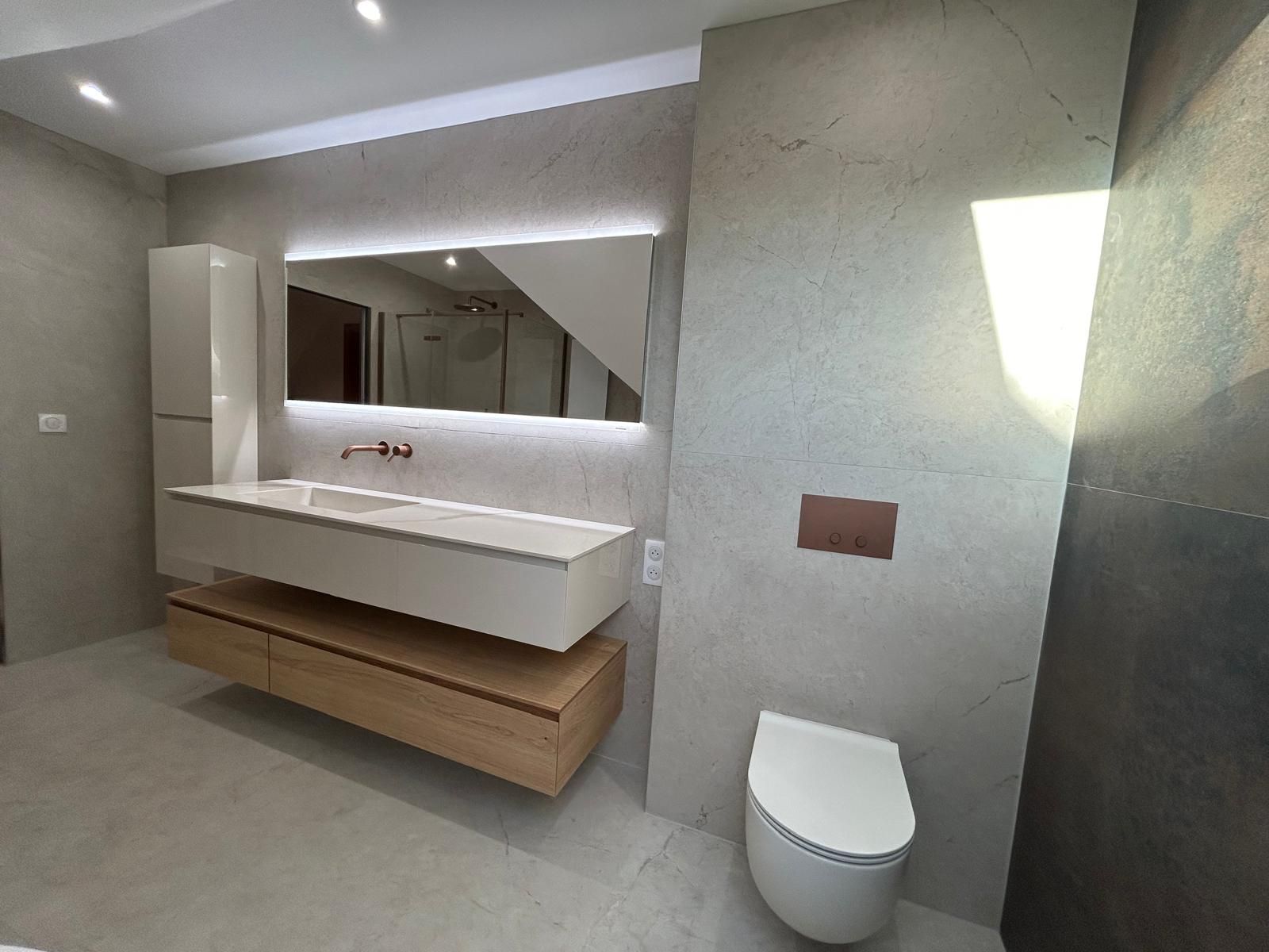 Salle de bain moderne avec meuble-lavabo suspendu, toilettes et grand miroir. Tons gris et bois.