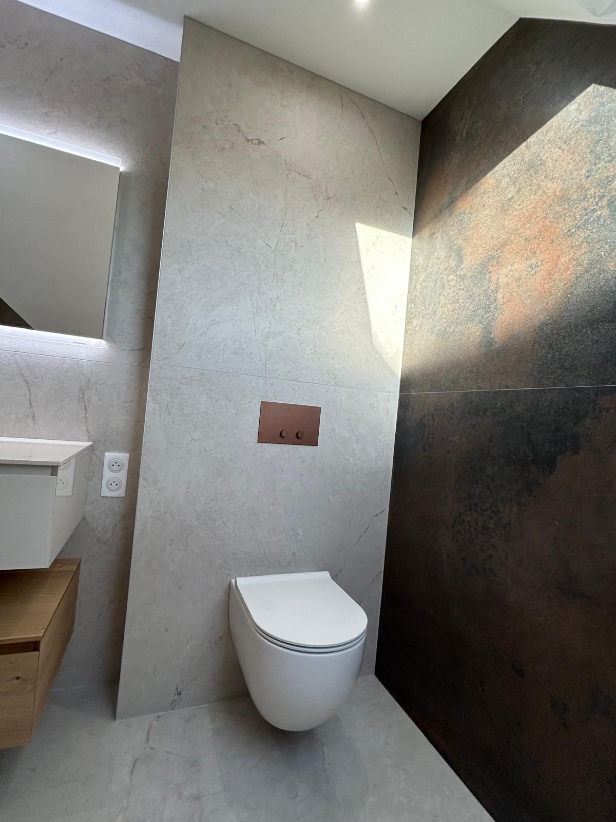 Salle de bain moderne avec toilettes blanches, mur gris texturé et mur marron foncé.