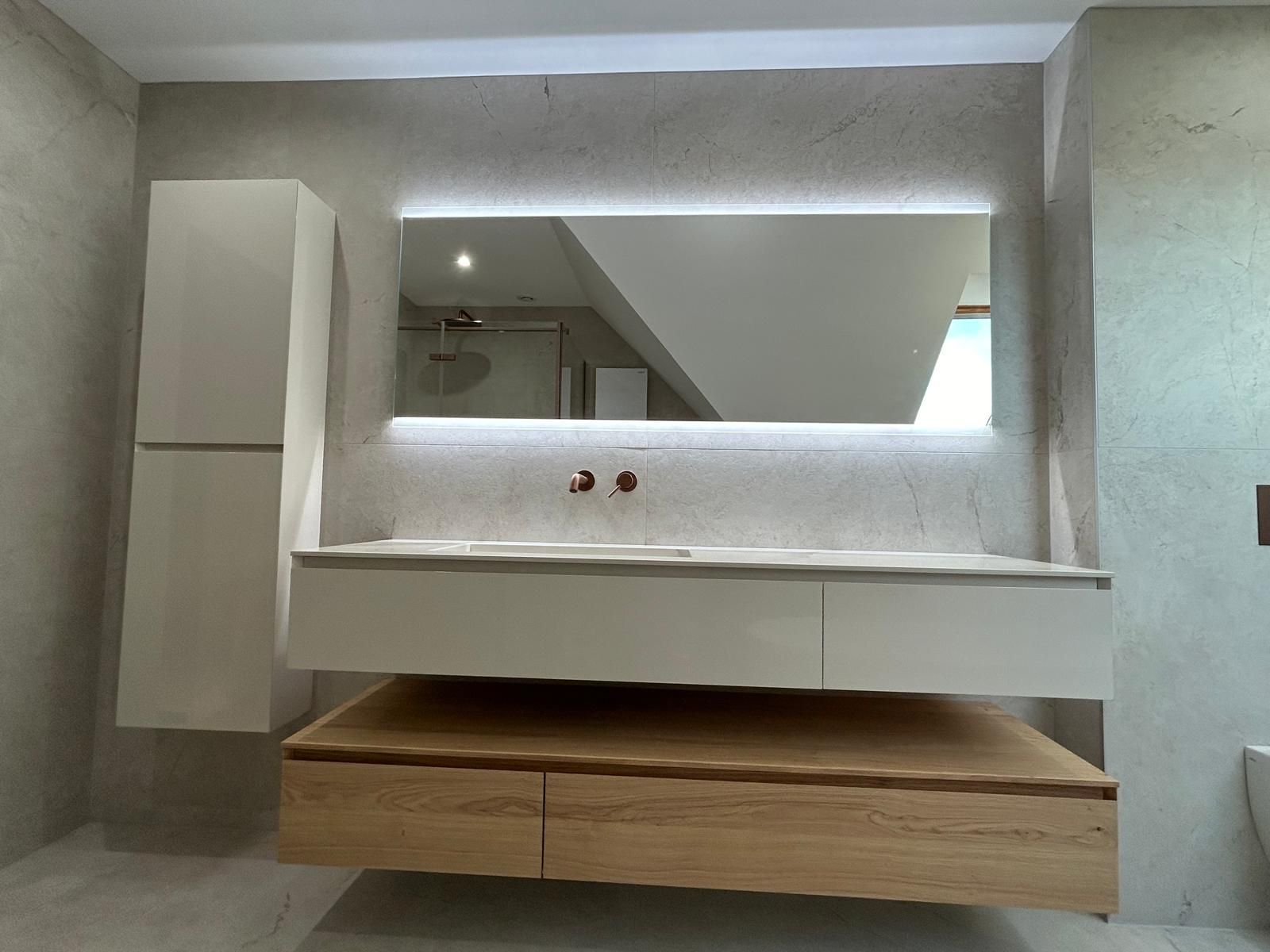 Salle de bain moderne avec vanité flottante en bois, armoires blanches et grand miroir avec rétroéclairage.
