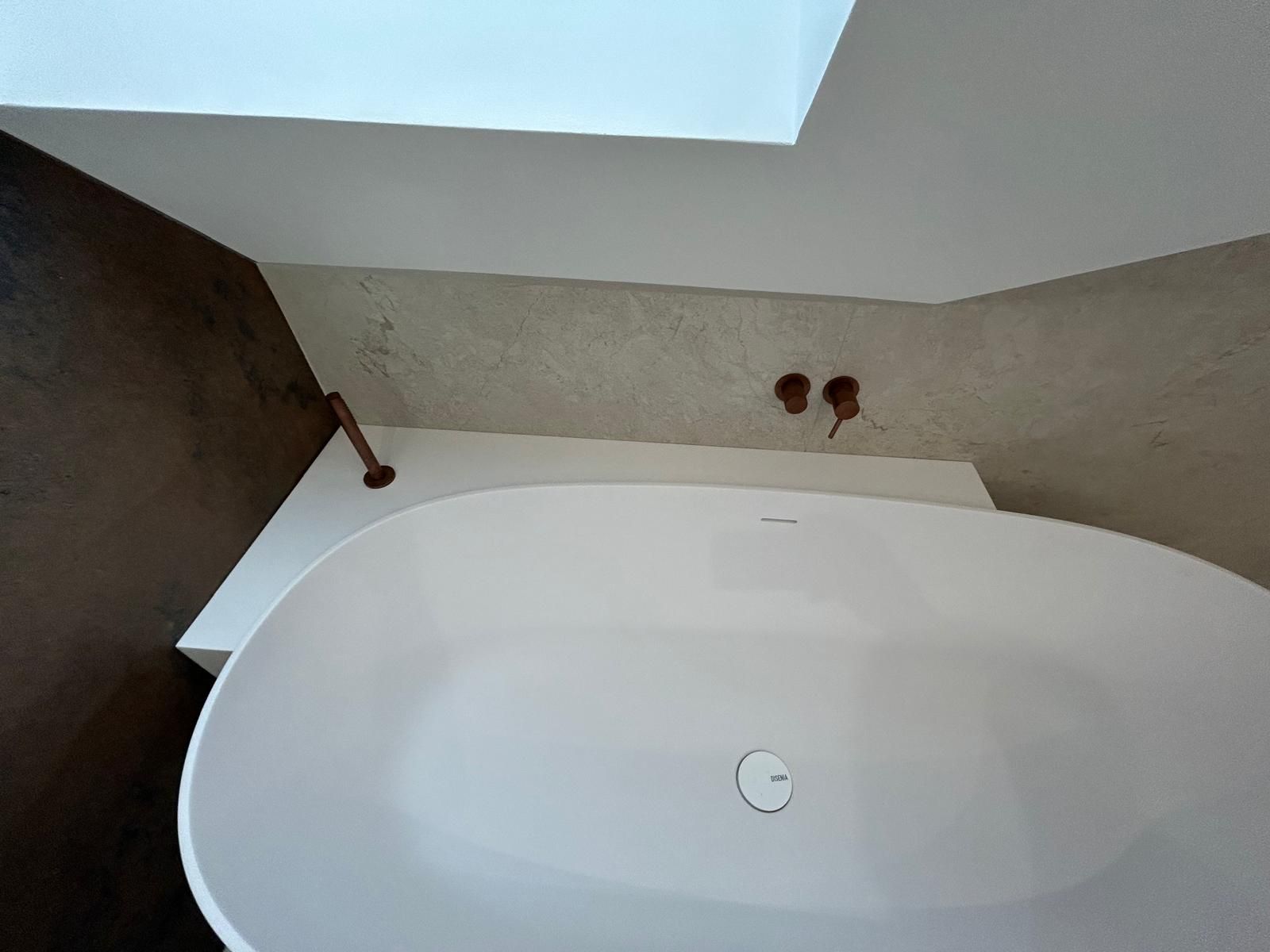 Une baignoire blanche installée dans une salle de bain minimaliste avec des accessoires en cuivre et une palette de couleurs neutres.