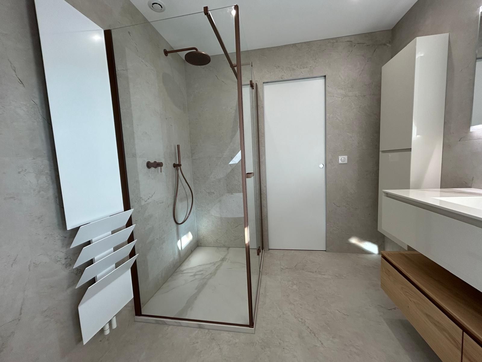 Salle de bain moderne avec douche en verre, armoires blanches et murs de couleur claire.