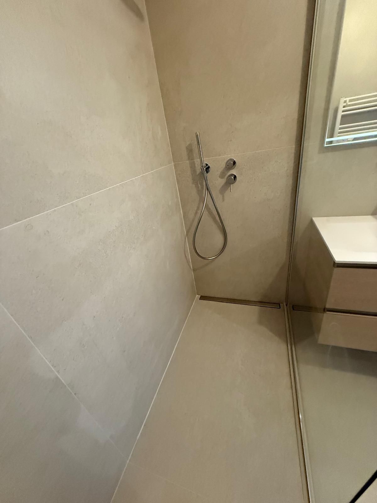 Douche avec murs en carrelage beige, luminaires chromés et vanité dans le coin.