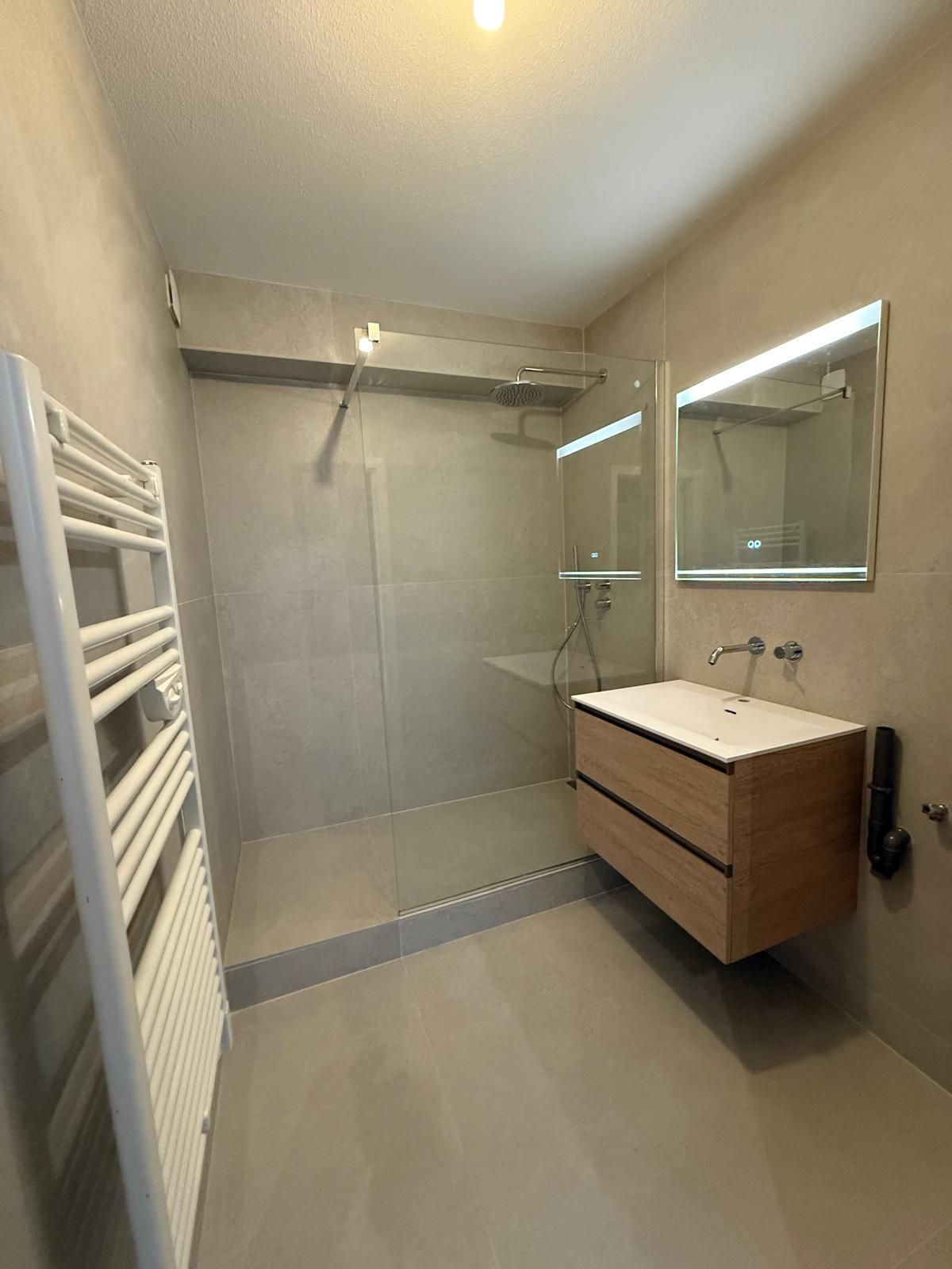 Salle de bain moderne avec murs gris, douche à l'italienne, vanité flottante en bois et porte-serviettes chauffant.