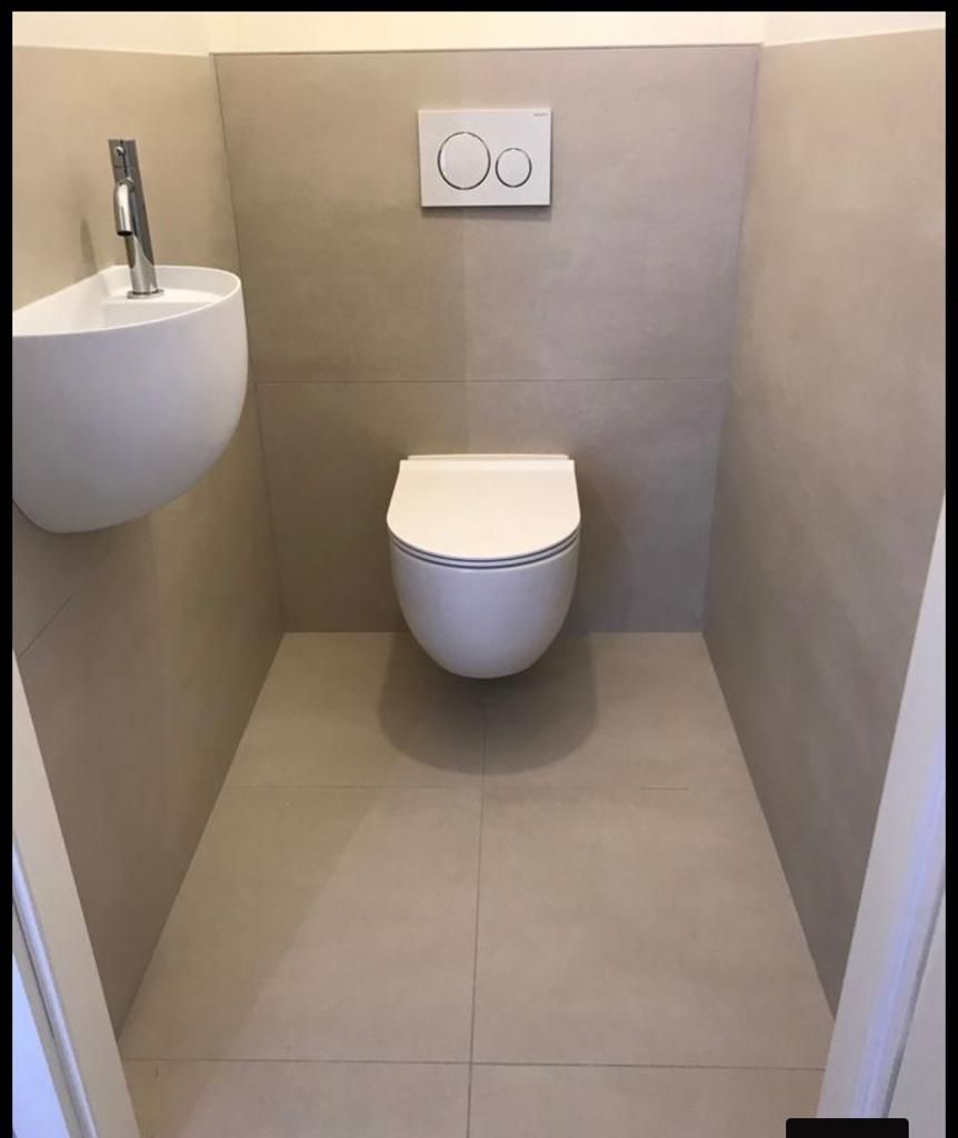 Petite salle de bain moderne avec toilettes suspendues et lavabo. Un carrelage beige recouvre les murs et le sol.