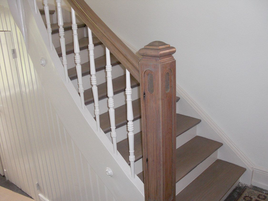 Un escalier en bois avec rampe et marches blanches dans une maison.