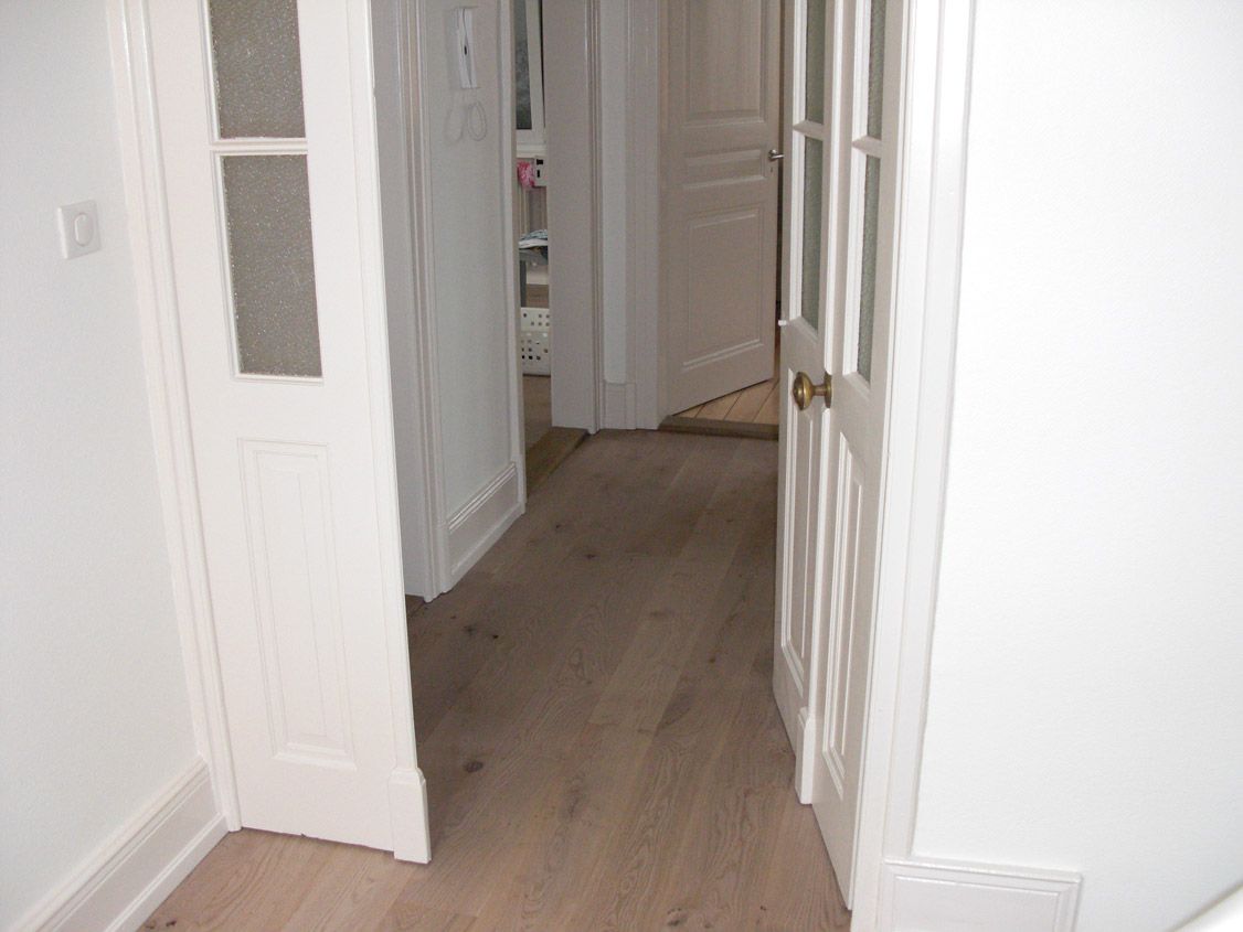 Un couloir avec parquet et portes blanches