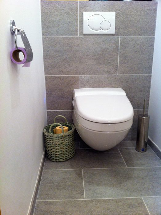 Salle de bain moderne avec carrelage gris, toilettes blanches et panier en osier avec papier toilette.