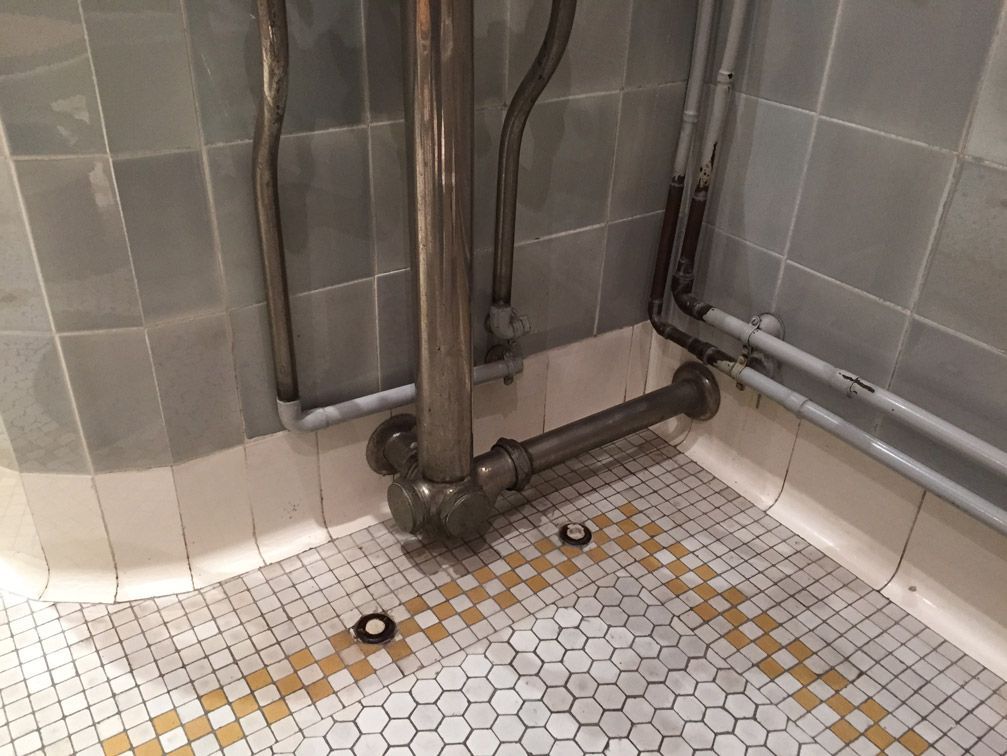 Une salle de bain avec un sol carrelé et des tuyaux au sol.