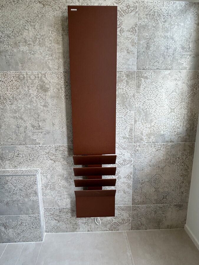 Un radiateur marron est accroché sur un mur carrelé dans une salle de bain.