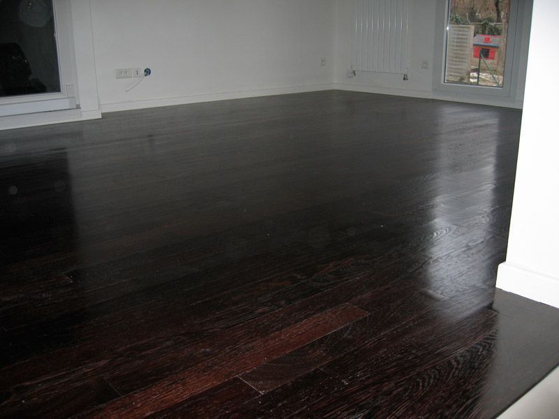 Une pièce vide avec un parquet en bois foncé et des murs blancs