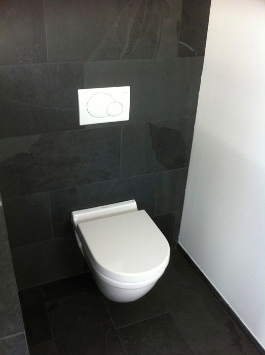 Toilettes blanches modernes avec un bouton à double chasse sur un mur carrelé noir.