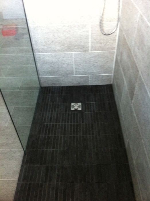 Une douche à l'italienne avec un sol en carrelage noir et une porte vitrée.