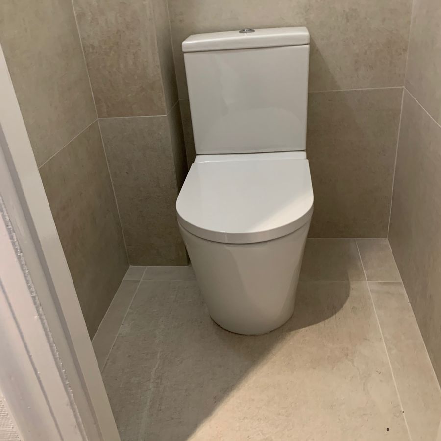 Des toilettes blanches sont posées sur un sol carrelé dans une salle de bain.