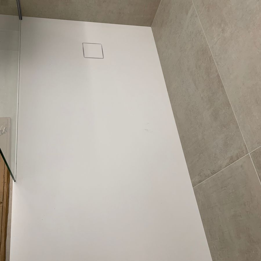 Une cabine de douche blanche dans une salle de bain avec un drain carré.