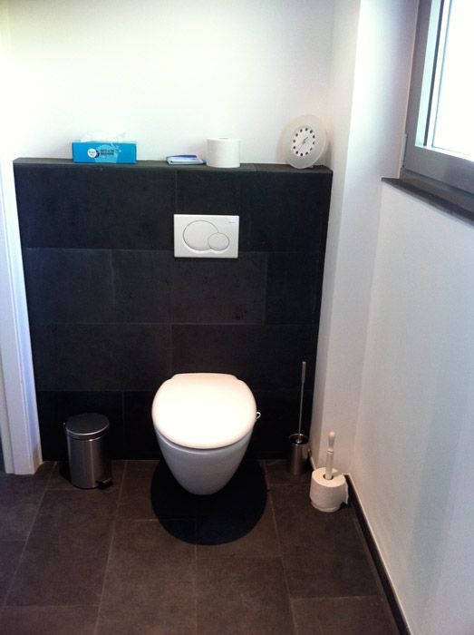 Des toilettes modernes avec du carrelage mural noir, un siège de toilette blanc et une poubelle en métal dans une salle de bain.