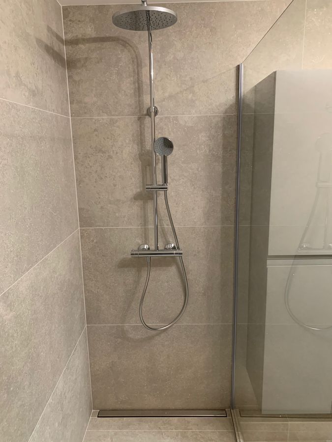 Une douche avec pommeau de douche et porte vitrée.