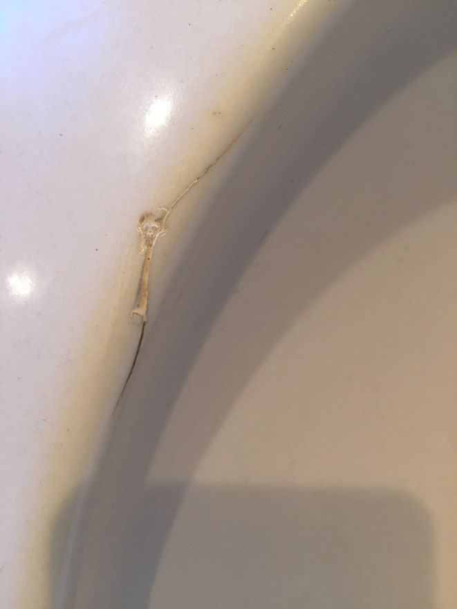 Gros plan d'une surface en céramique blanche fissurée, avec une petite formation en forme de bulle de couleur dorée près de la fissure.