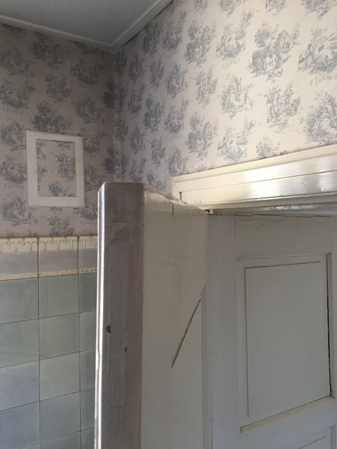 Une porte est ouverte dans une pièce avec un papier peint floral sur le mur.