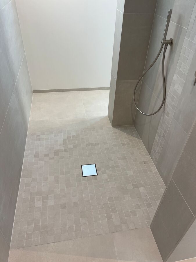 Une douche à l'italienne avec un sol carrelé et une pomme de douche.