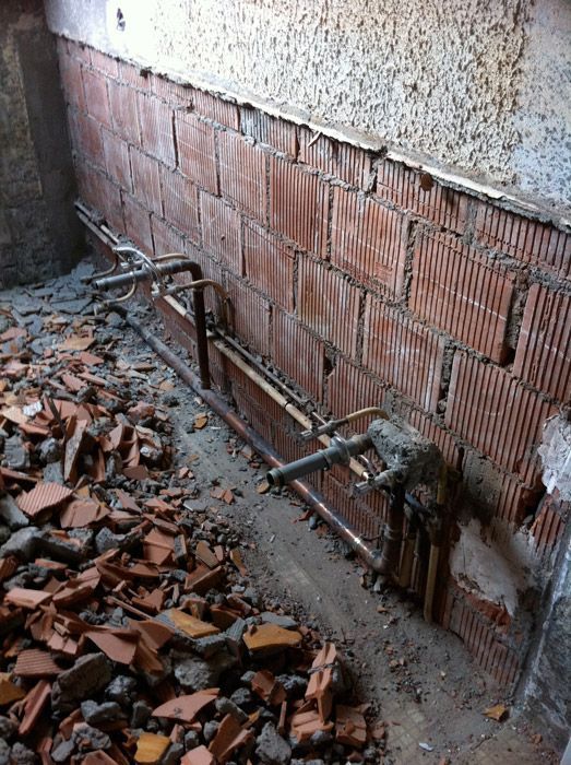 Un mur de briques est en train d'être démoli et il y a un tas de pierres sur le sol.