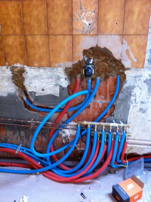 Un tas de tuyaux bleus et rouges sortant d'un trou dans un mur