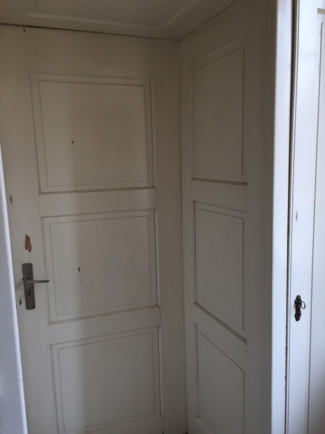 Une porte blanche avec une poignée noire se trouve dans un coin d'une pièce.