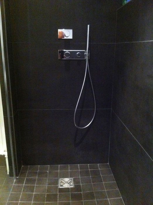 Une douche avec un sol en carrelage noir et une pomme de douche chromée