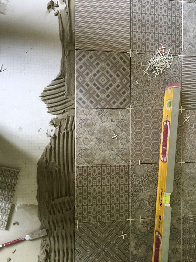 Un sol carrelé est en cours d'installation avec un niveau et une spatule.