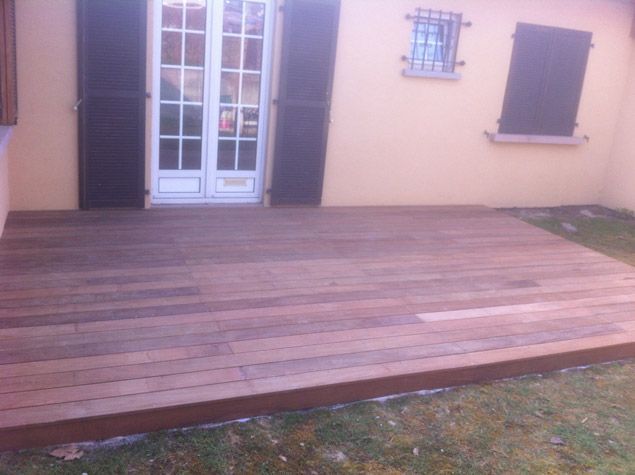 Une terrasse en bois devant une maison avec une fenêtre et des volets.