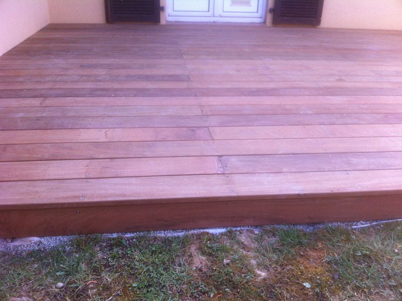 Une terrasse en bois est assise dans l'herbe devant une maison.