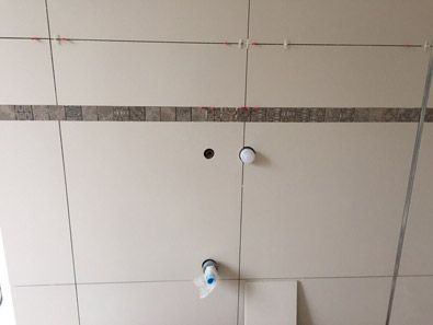 Un mur de salle de bain avec du carrelage en cours d'installation et un trou dans le plafond.
