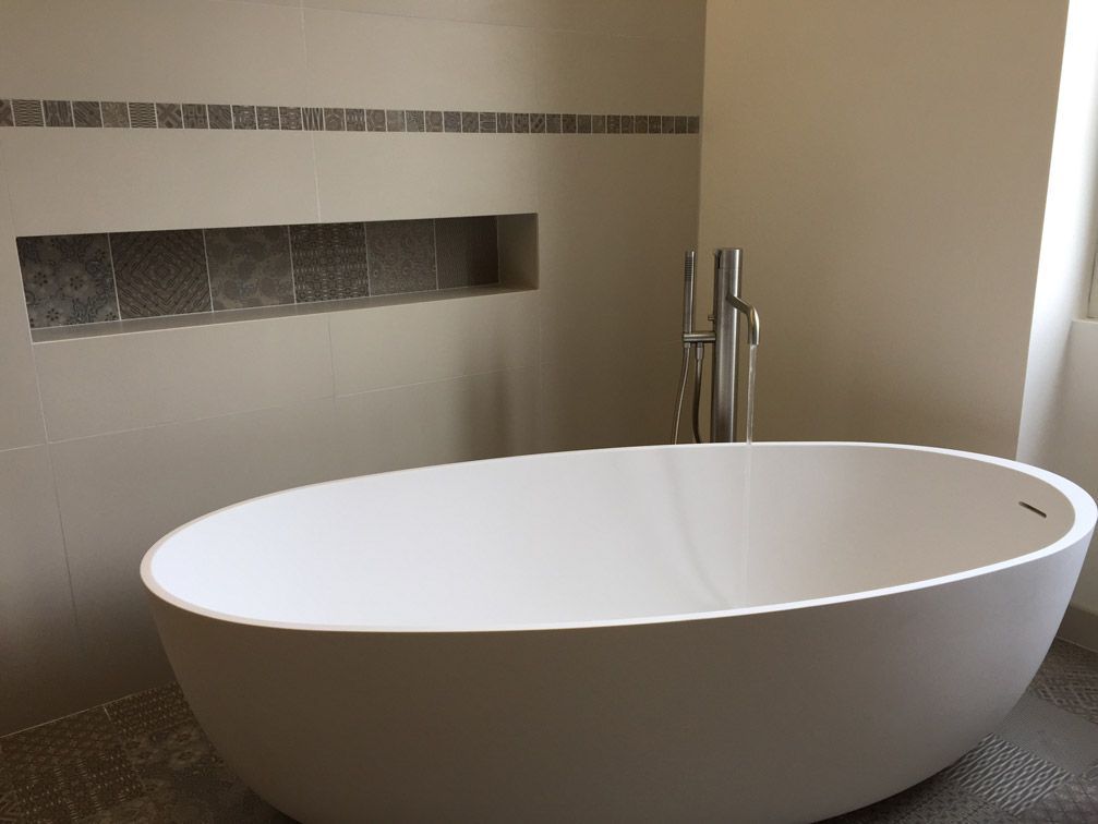 Une baignoire blanche est posée dans une salle de bain à côté d'un mur.