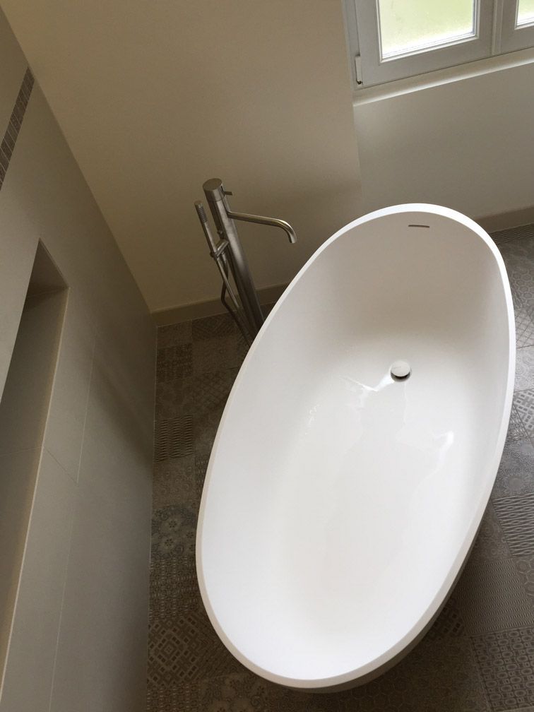 Une baignoire blanche se trouve dans une salle de bain à côté d'une fenêtre.