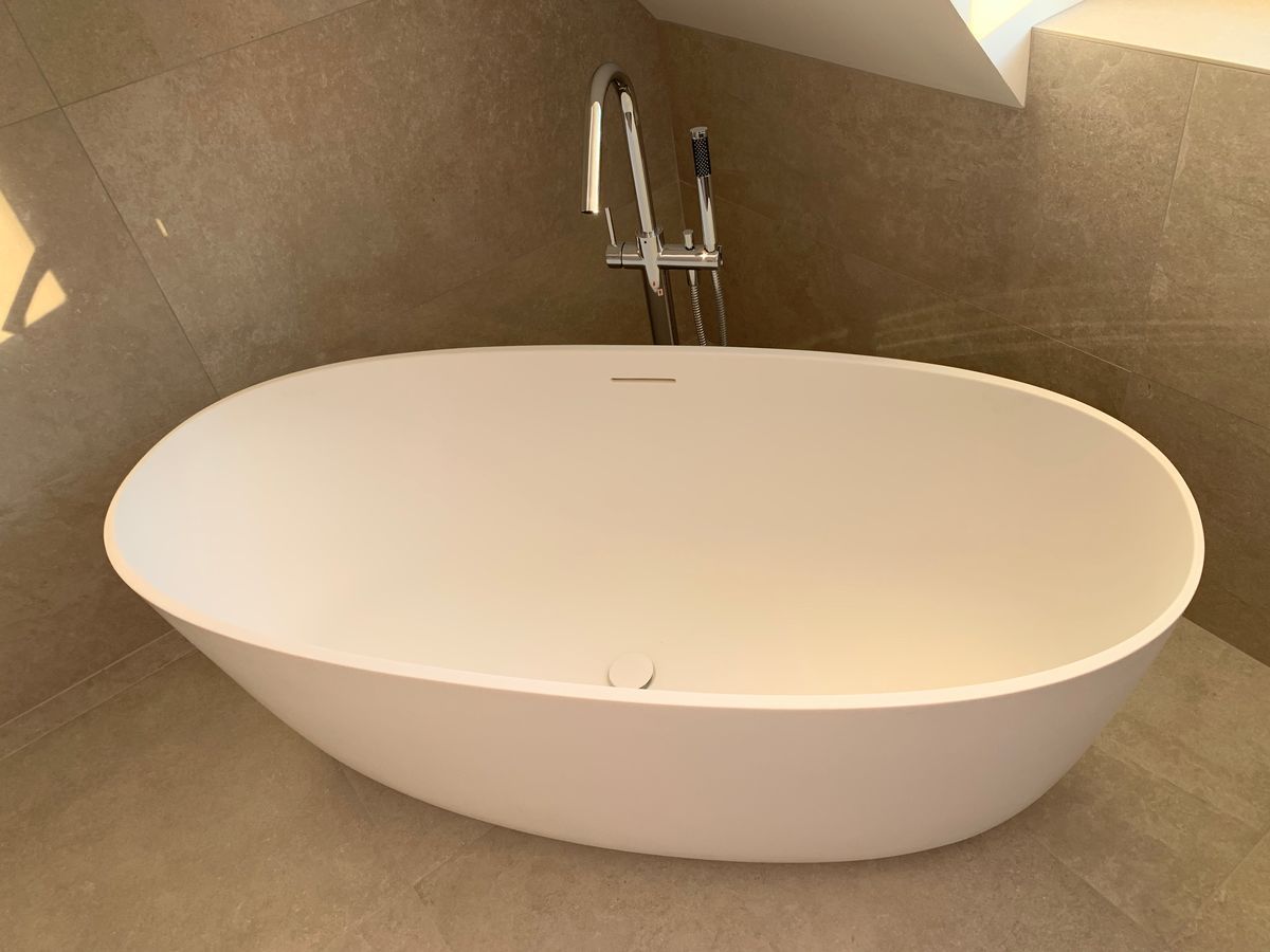 Une baignoire blanche est posée sur un sol carrelé dans une salle de bain.