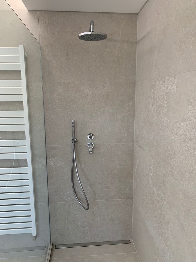 Une douche avec pommeau de douche et un porte-serviettes blanc.