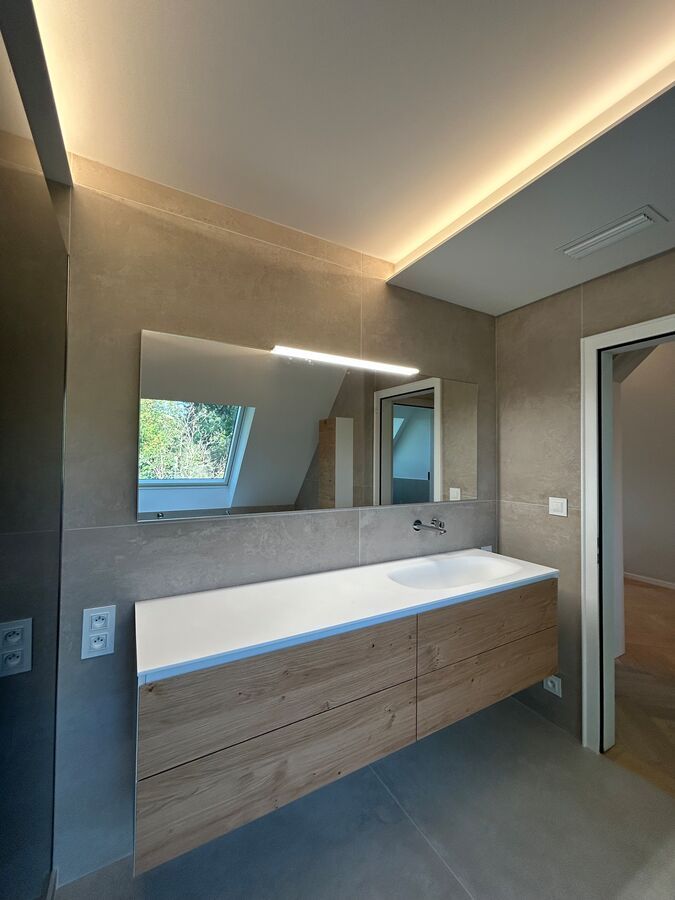 Une salle de bain avec lavabo, miroir et puits de lumière.