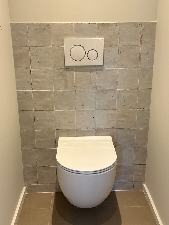 Des toilettes blanches sont posées sur un mur carrelé dans une salle de bain.