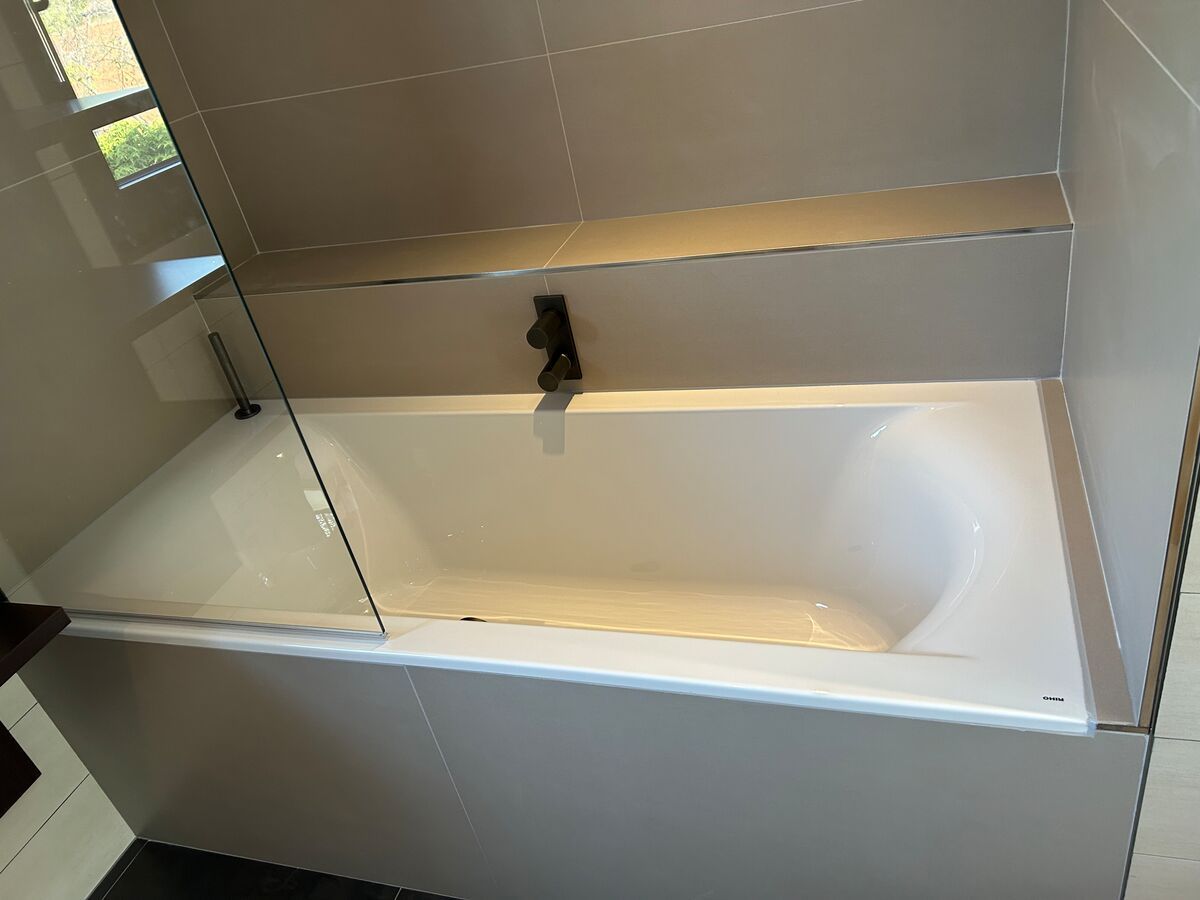 Une baignoire dans une salle de bain avec un robinet noir et une porte vitrée.