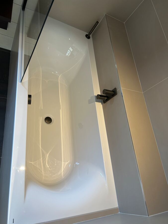 Une baignoire blanche est posée dans une salle de bain à côté d'un mur carrelé.