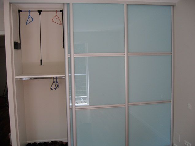 Un placard avec portes coulissantes en verre et cintres.
