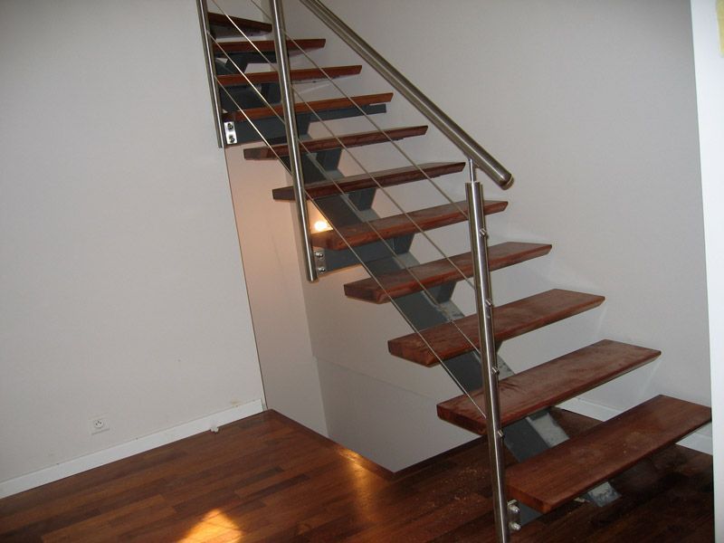 Escalier en bois avec rampe en métal et marches ouvertes; marches brunes, murs blancs, plancher en bois.