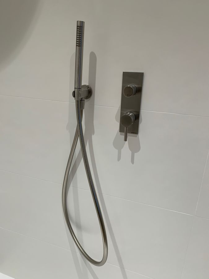 Une pomme de douche avec un tuyau attaché est accrochée à un mur blanc.