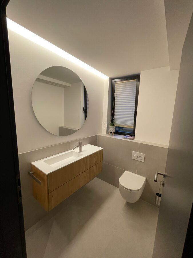 Une salle de bain avec lavabo, WC, miroir et fenêtre.