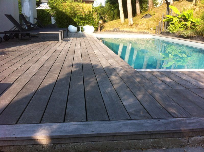 Une terrasse en bois avec une piscine en arrière-plan