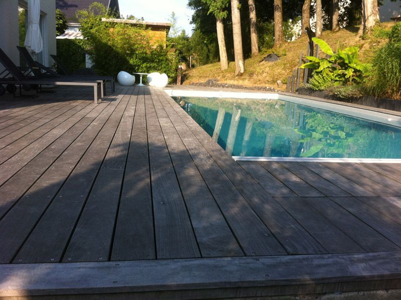 Une terrasse en bois avec une piscine en arrière-plan