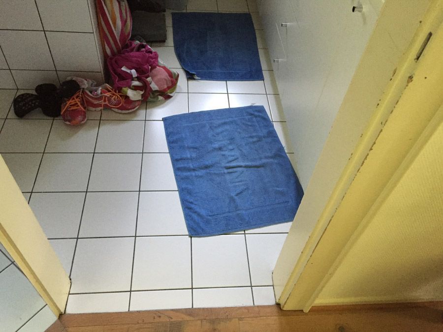 Une salle de bain avec du carrelage blanc et des serviettes bleues au sol