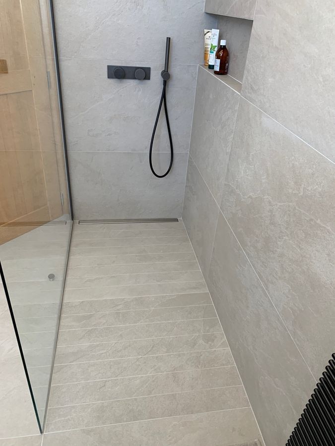 Une salle de bain avec une douche à l'italienne et une étagère avec des bouteilles dessus.